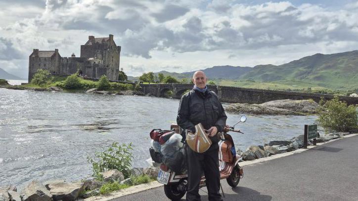 A biker with a scooter in front of Ellan Donan Castle in the Highlands