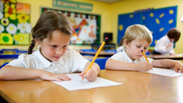 A girl sat in a classroom writing with her left hand, sat next to a right-handed boy.