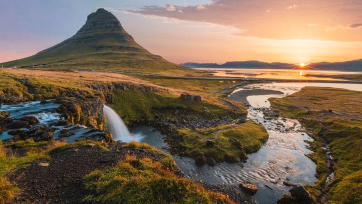 A picture of the Iceland landscape at sunset, showing a small waterfall and mountains in the background.
