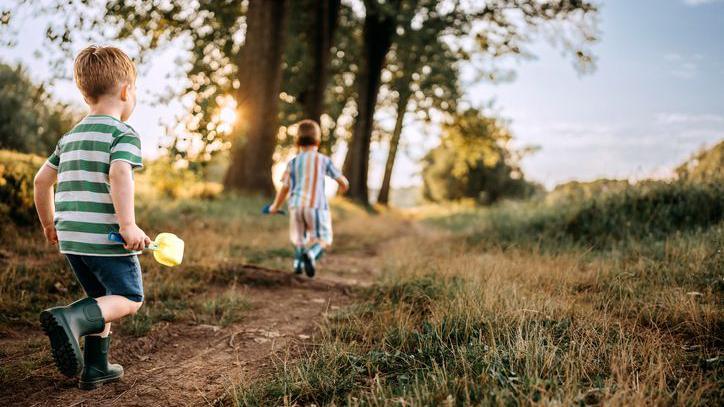 Two boys walking, one a few metres in front of the other.