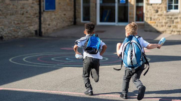 Two boys running to school with backpacks on.