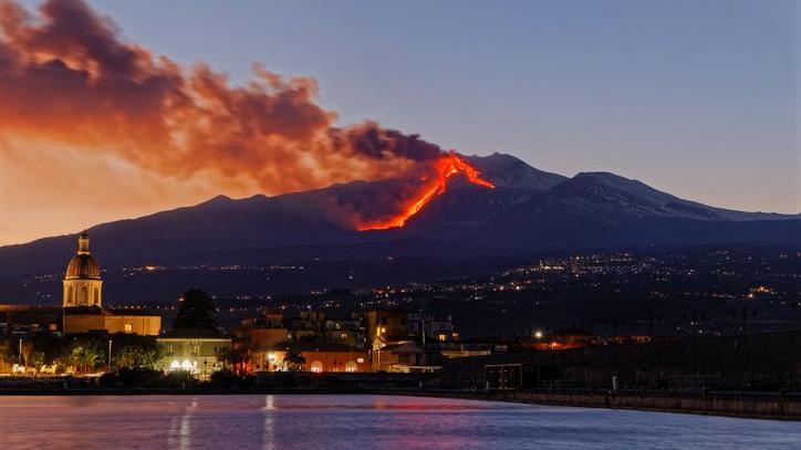 A picture taken at night of Mount Etna whilst it's erupting, with bright orange lava flowing down the volcano.