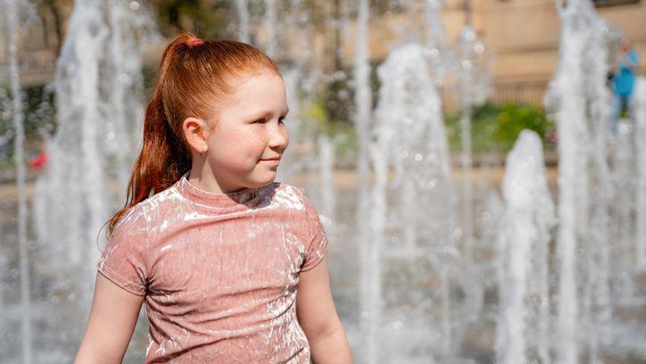 Young girl enjoys playing in fountain on a sunny day.