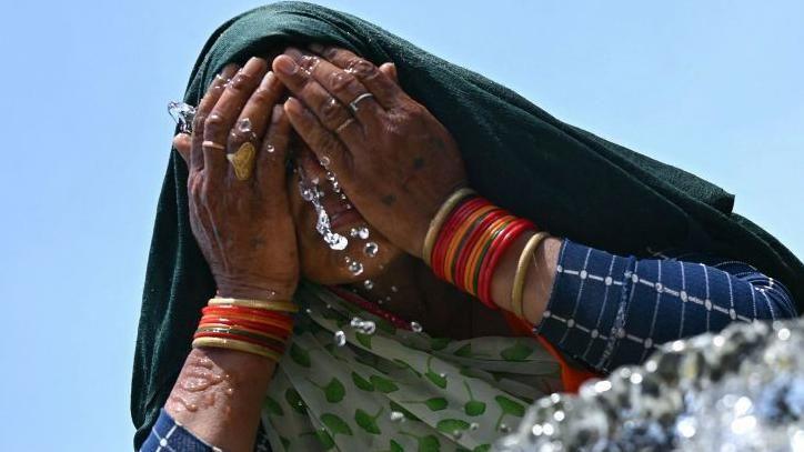 A woman washes her face with water to cool off during a hot summer day near the India Gate in New Delhi on June 17, 2024. 