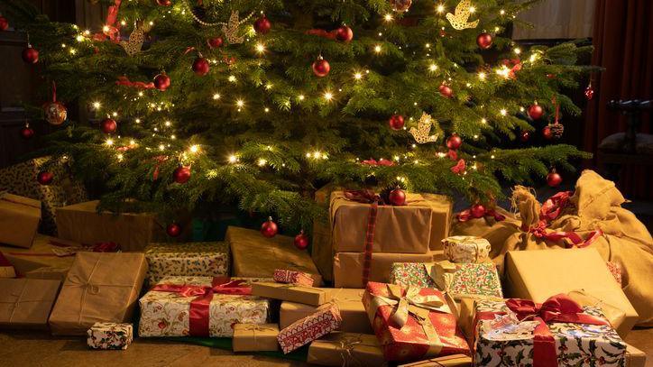 A Victorian-style Christmas tree with white lights and red decorations and traditionally-wrapped presents underneath.