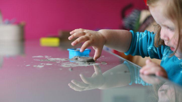 A child concentrating on playing with moulding clay on reflective table.