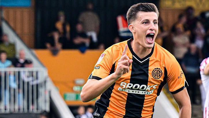 Kell Watts runs off in celebration wagging his right finger after scoring a goal for Cambridge United