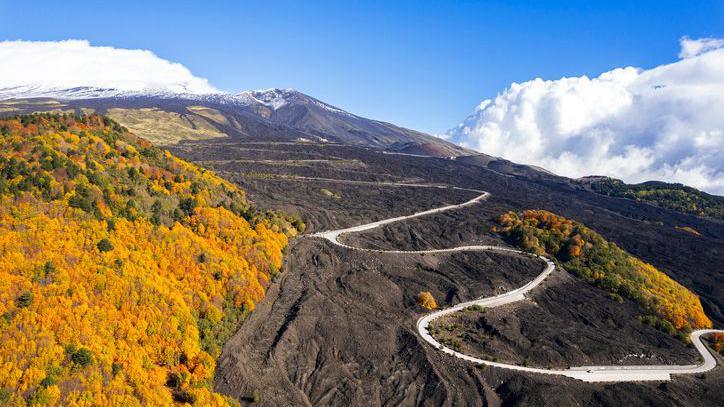 A winding road on black lava terrain heading towards Mount Etna.
