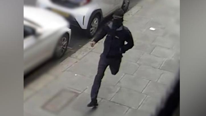 CCTV image of a man dressed in black wearing a hat and with his face covered running down the street 