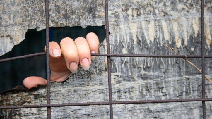 A hand of someone kept in solitary confinement showing through a crack in a wooden board