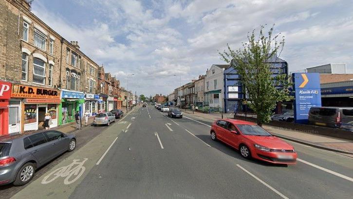 A Google Street View of Spring Bank, Hull. There are several cars coming towards the the camera and none on the other side. There is a Kwik Fit on the right and several shops on the left next to a bike lane