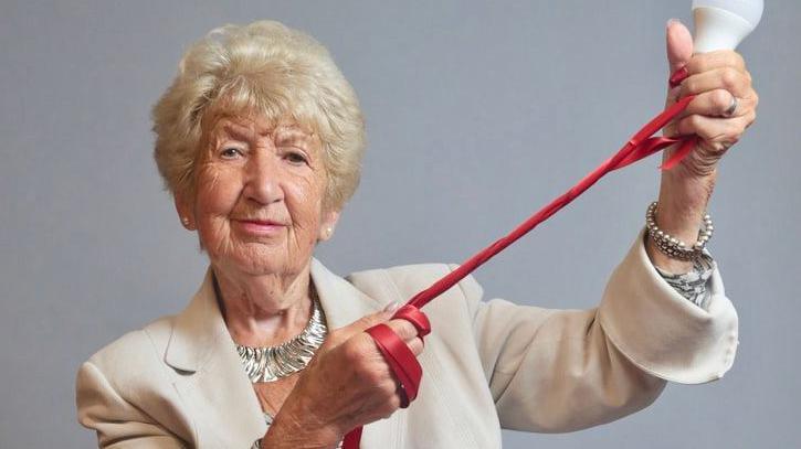 Norma Glass is holding a lightbulb, symbolic of the light celebrated during the festival of Hanukkah. She's wearing a cream blazer and silver jewellery. 