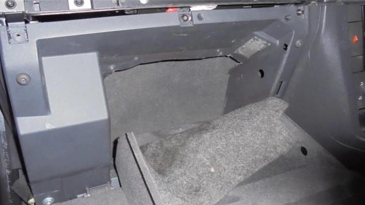 A modified compartment, or hide, in the footwell of a black car. A panel has been removed showing a small space where the gang hid people. 