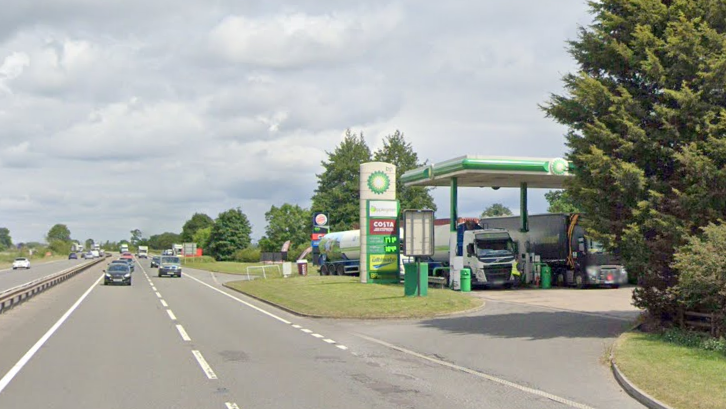 A dual carriageway is pictured with a service station and lorries to the right of the image