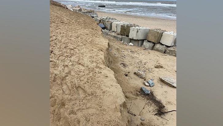 Exposed large rocks used to prevent coastal erosion on a sandy beach with the sea in the background