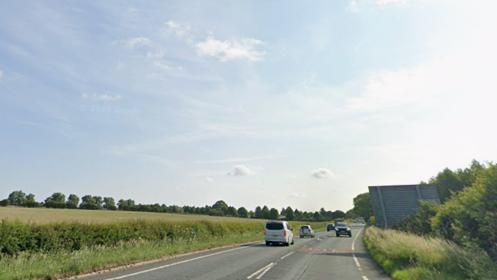 Road with a field to the left of the image, with blue sky above