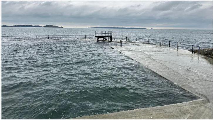 The diving board is pictured at high tide against a grey sea and grey sky.