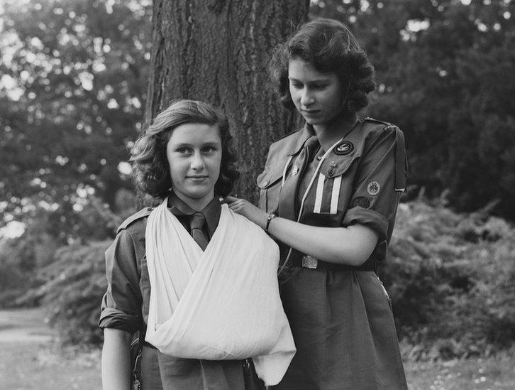 Princess Elizabeth places Princess Margaret's arm in a sling as part of the girl guides in Frogmore, Windsor, England on 11 April 1942