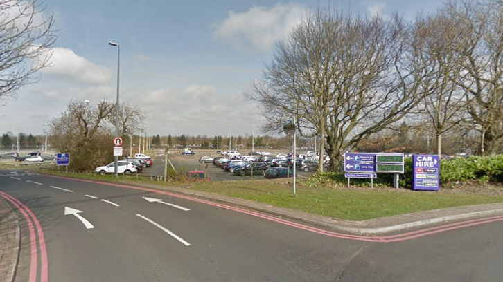 Newcastle International Airport Short Stay 2 car park. There are double red lines and road markings leading to the car park, with dozens of cars parked inside.