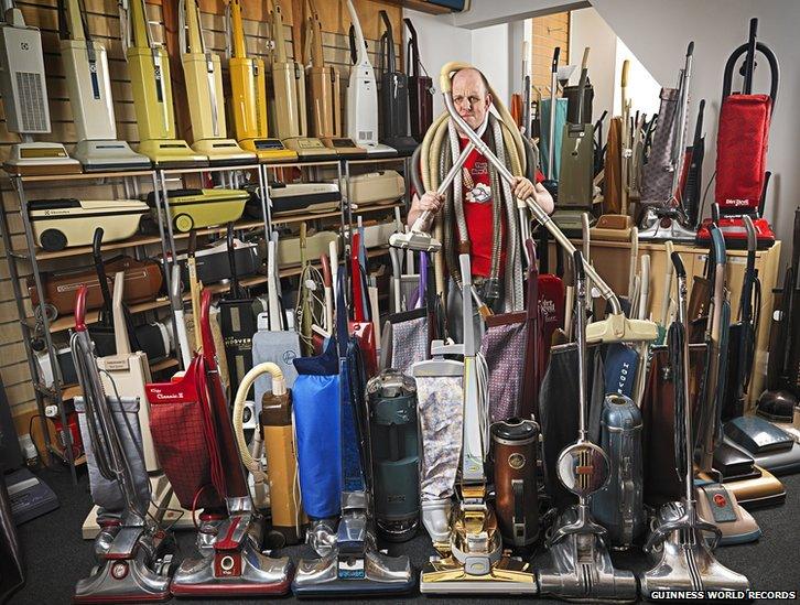 A man stood among a collection of vacuum cleaners.