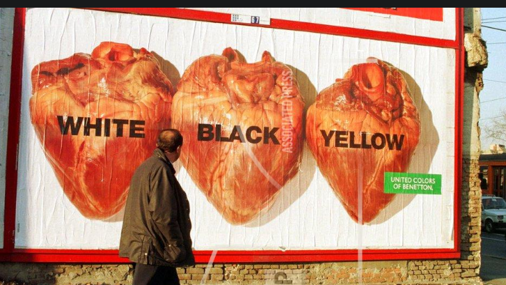 A man walks past a billboard depicting three human hearts labelled white, black and yellow. 