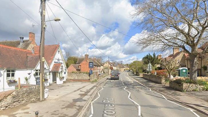 Road through a village with a white pub on the left and homes to the right.