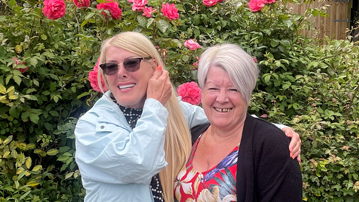 Heather - with blonde hair and a light blue jacket - and Marian - with white hair and wearing a flowery dress and a black jumper - both smiling for the camera 