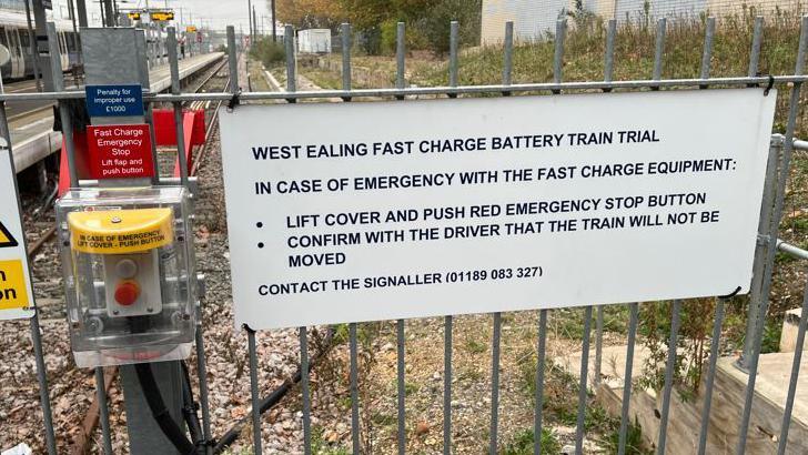 A sign on a fence at a station signifies the battery train trial is under way. 