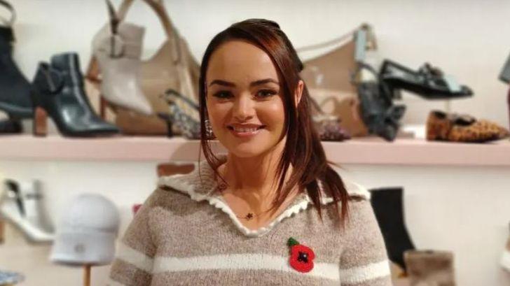Rachel is wearing a poppy and a brown and cream jumper. She has her hair tied up. There are shoes behind her.