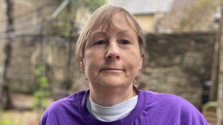 Ruth Strange wearing a purple top and looking serious as she looks at the camera. The background is blurred but you can just see the Silver Birch trees she wants to protect.
