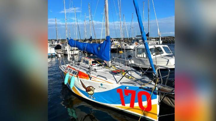 Little Wren in the water at a marina. The small sailing boat is white with a blue and yellow stripe and the number 170 in red on the side. It also has a drawing of a bird on the side of it.