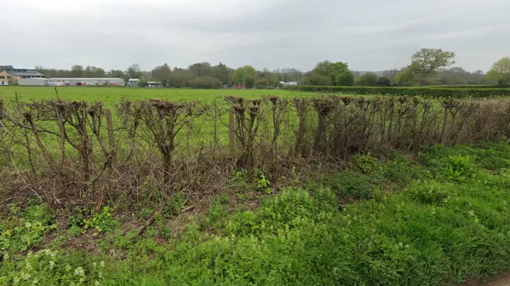 Fields and hedges south east of Newent, with buildings in the distance. 