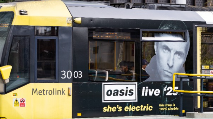 A yellow Manchester tram with a photo of Liam Gallagher underneath an Oasis sign