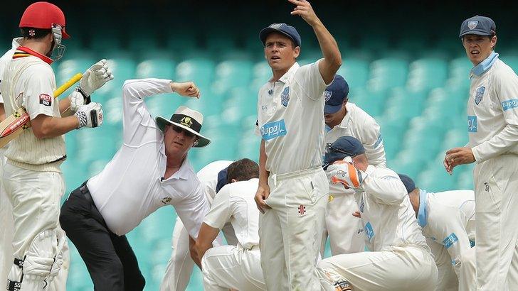 Players surround Phil Hughes on the field in Sydney
