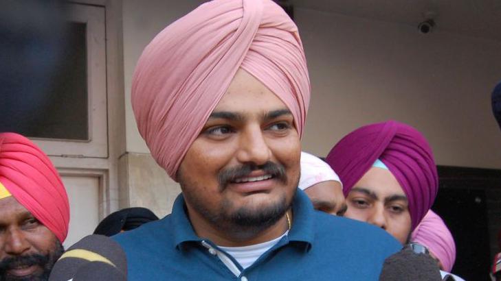 Sidhu Moose Wala pictured in 2020. Sidhu is an Asian man with a pale pink turban, short moustache and a beard. He wears a blue polo shirt.