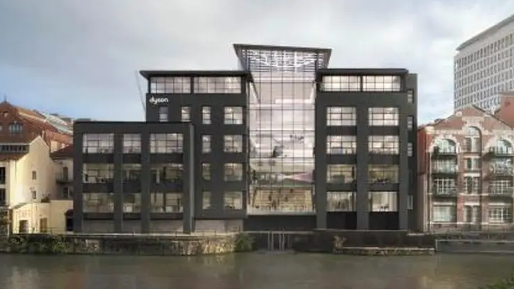 An image of a large office on the Bristol water front with many glass windows and black cladding, flanked either side by older, brick buildings. 