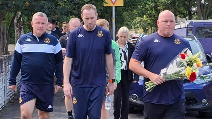 Southport manager Jim Bentley (right) and his players and staff walk from the clubs's ground on Haig Avenue to place flowers at the police cordon on nearby Hart Street