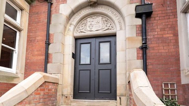 The door to the venue with an inscription above it which reads Tyne Improvement Commission River Police Station. It is a brick built building with an ornate door 