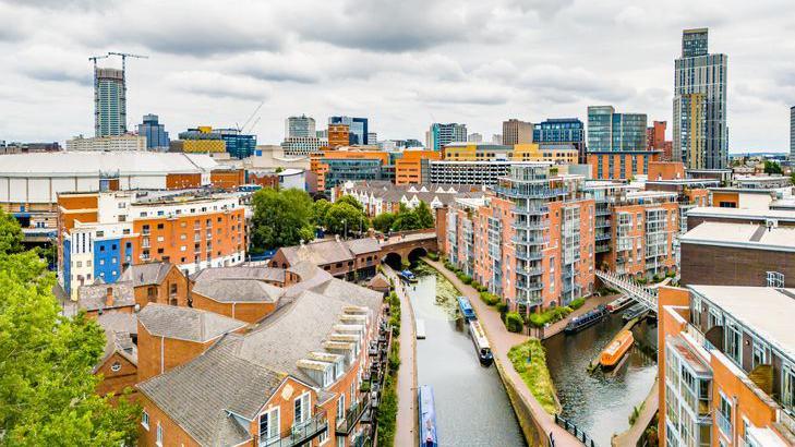 The Birmingham Canal Old Line in the city centre has barges on the water and apartment blocks and other buildings surrounding the waterways.