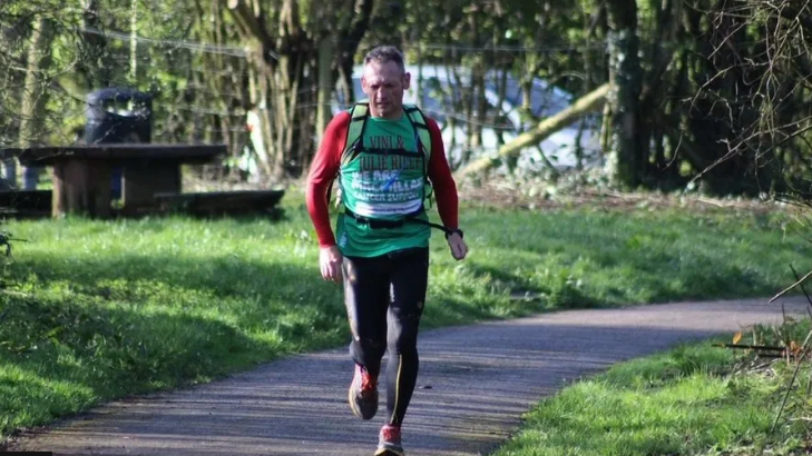 Gary McKee running in a park with large green verges on either side and trees behind with a car in the distance.