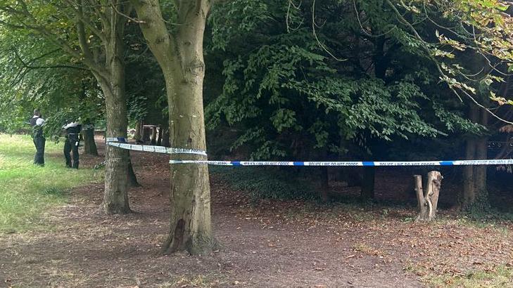 Photo of the police cordon around trees in Rosehill Park, with two uniformed officers standing nearby