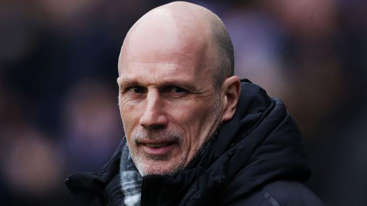 Philippe Clement has a grey stubble, shaved head and is wearing a black coat and checked scarf. He is slightly smiling with his head turned towards the camera.