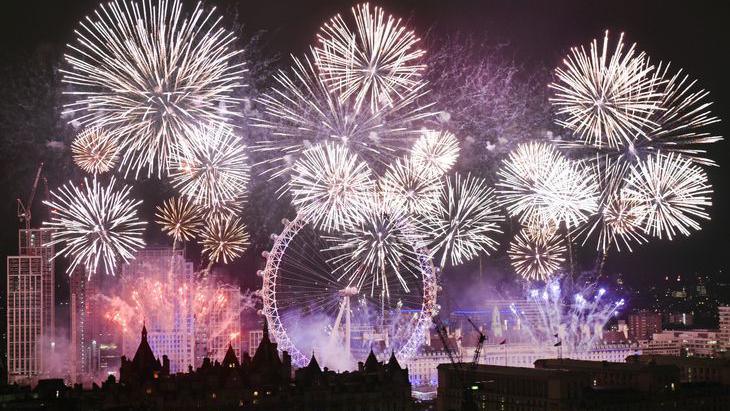 Fireworks skyline in london at new year - The London Eye is lit up surrounded by white explosions along the River Thames