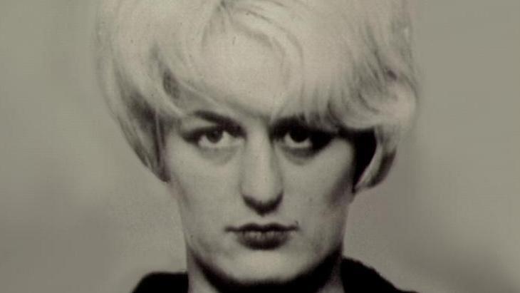A black and white police mugshot of Myra Hindley,  a woman with large white hair