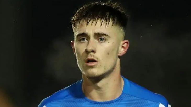 A football player with dark hair and wearing a blue shirt looks onto the pitch