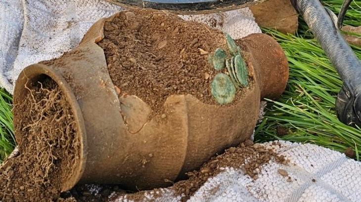 A clay pot with discoloured coins coming out of it.