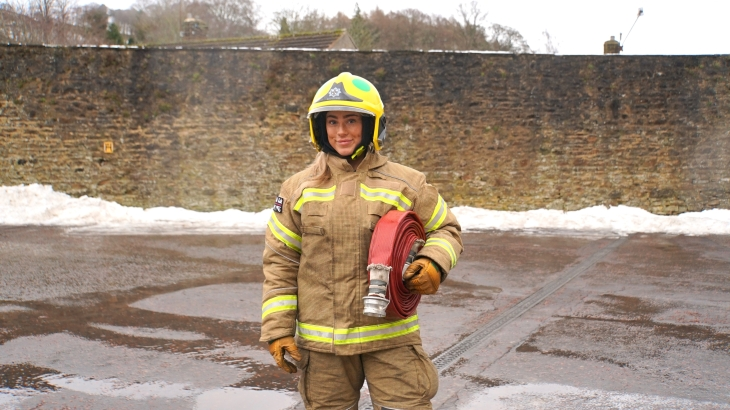 Mya Malthouse is standing holding a firehose under her arm. She's 20 years old and is wearing a firefighter's uniform.