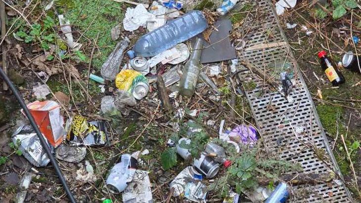 Cans, bottles, Crisp Packets and other mess on the floor next to a grid. 