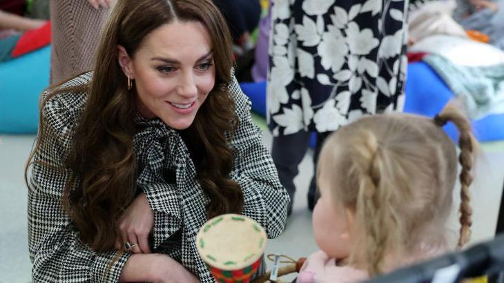 The Princess of Wales smiling with a small white girl with blonde hair and pigtails