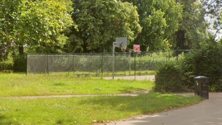 Unmown grass areas lead to a fenced off basketball court.